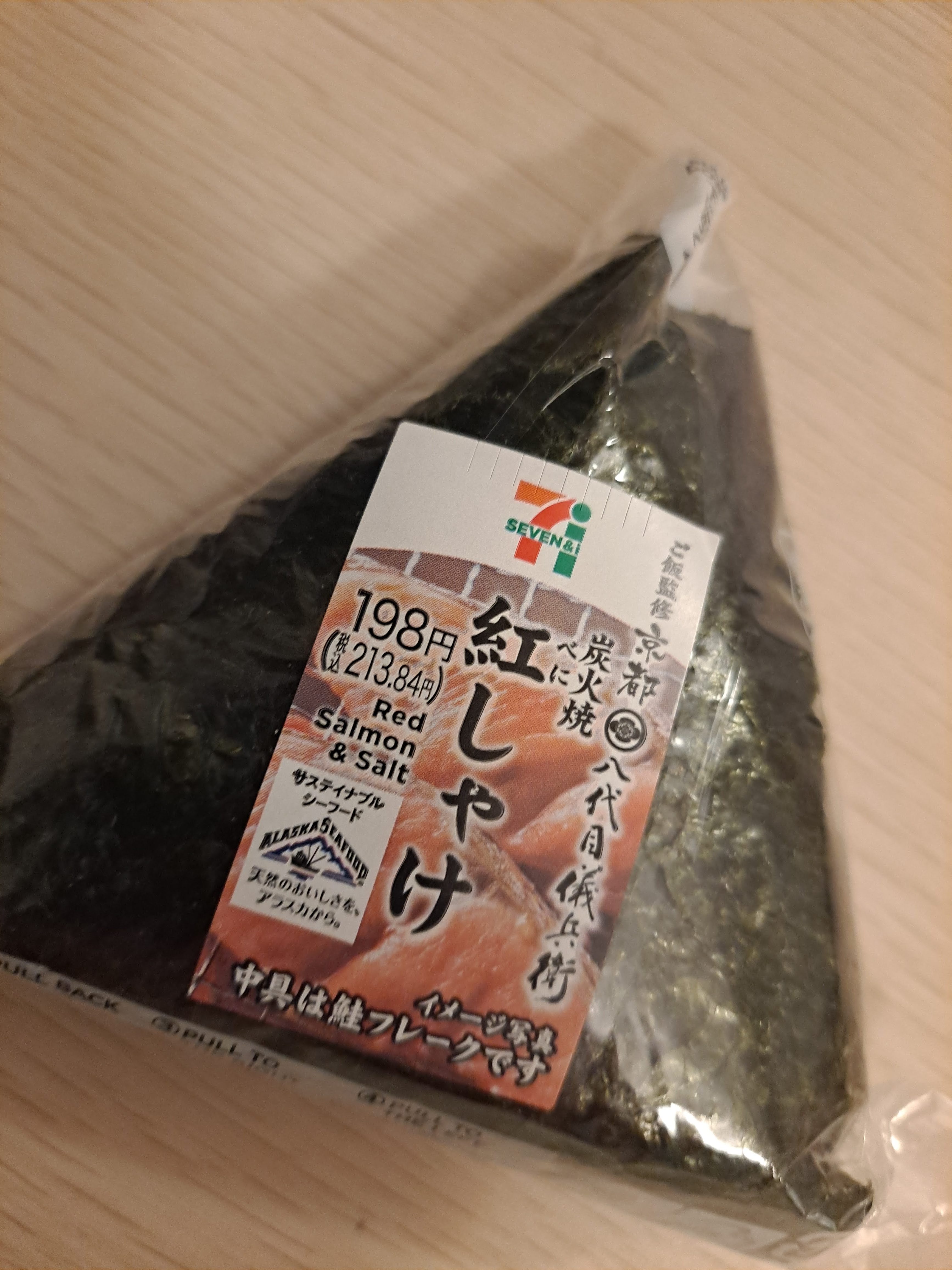 A packaged onigiri (rice ball) featuring red salmon and salt, wrapped in nori, from 7-Eleven.